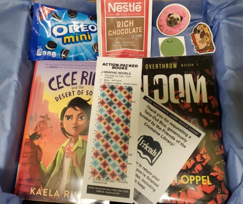 Assortment of items (books, stickers, snacks, etc) included  in a take-out box. 